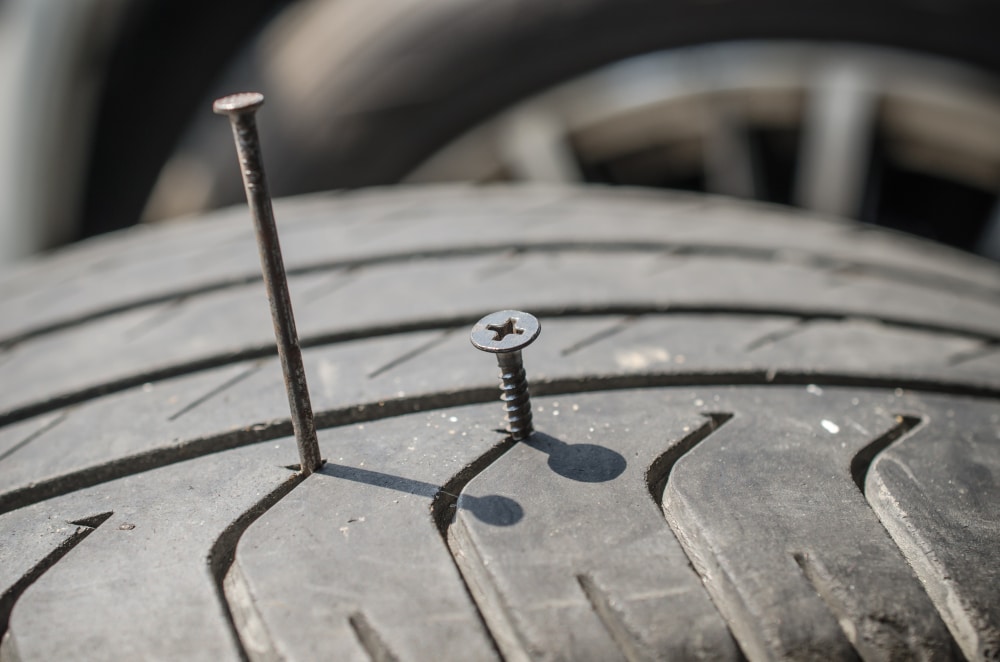 Close-up of a screw and a nail puncturing a tire.