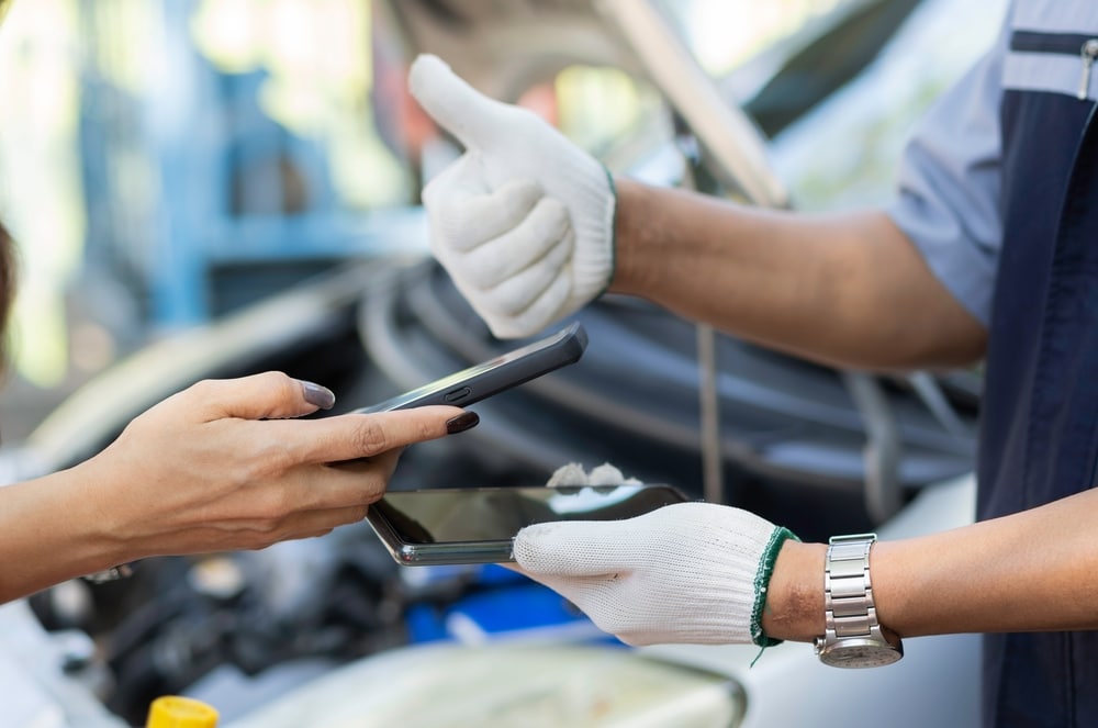 Close-up of auto mechanic exchanging contact info with a customer after a successful repair job.